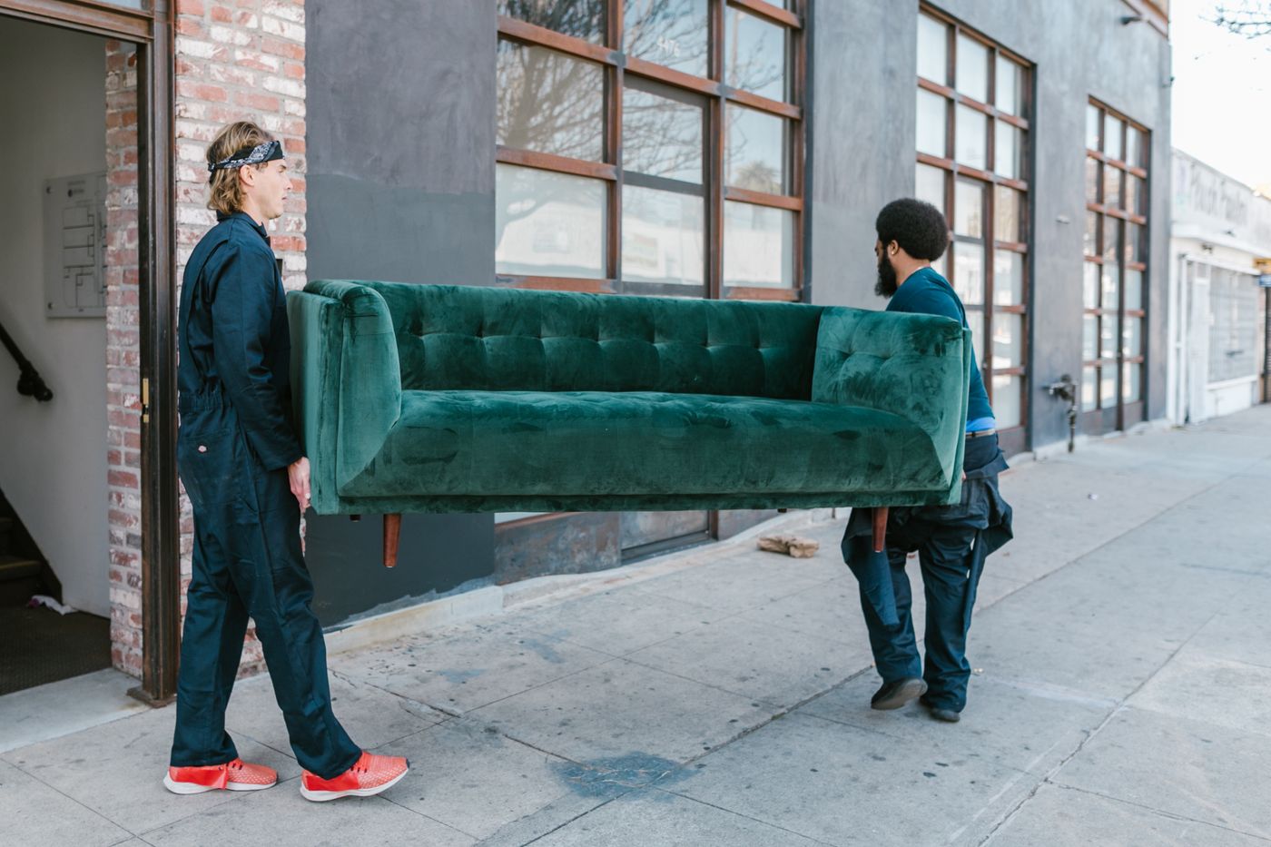 Two people carrying a sofa outside, illustrating bulky furniture removal